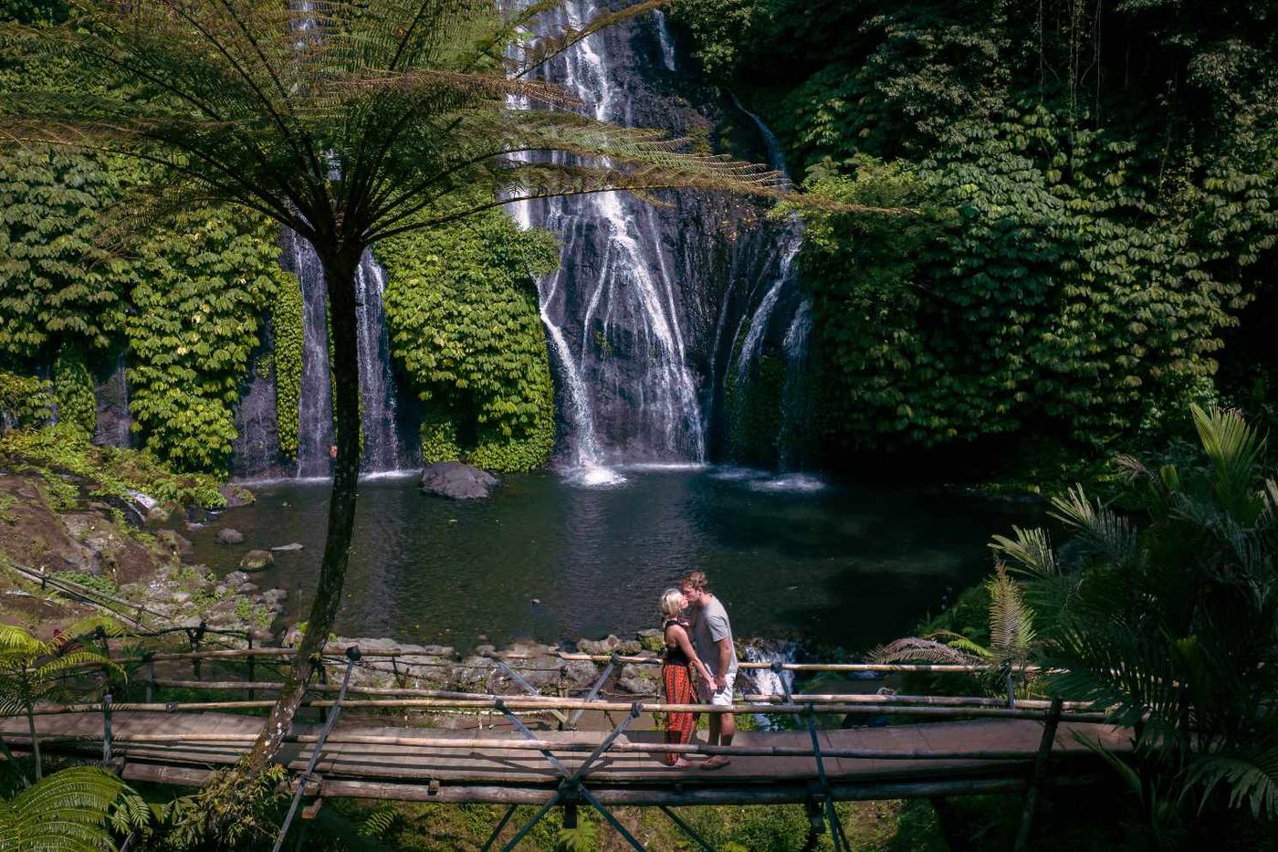 Twin waterfall falling into a jungle pool, with a visitor below