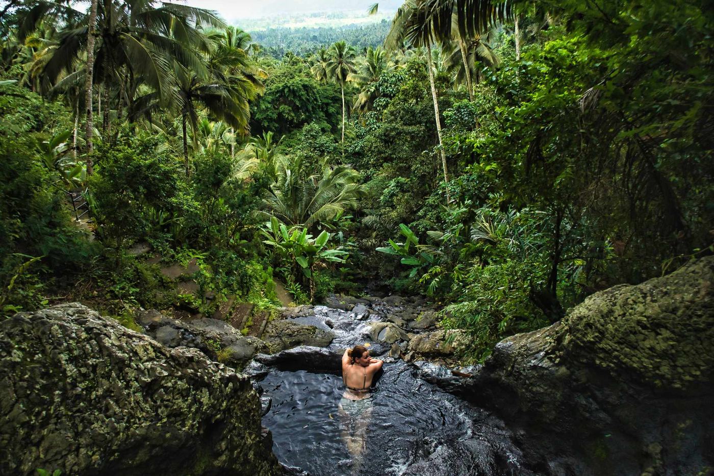 Swimmer in a river pool at the foot of a jungle gorge