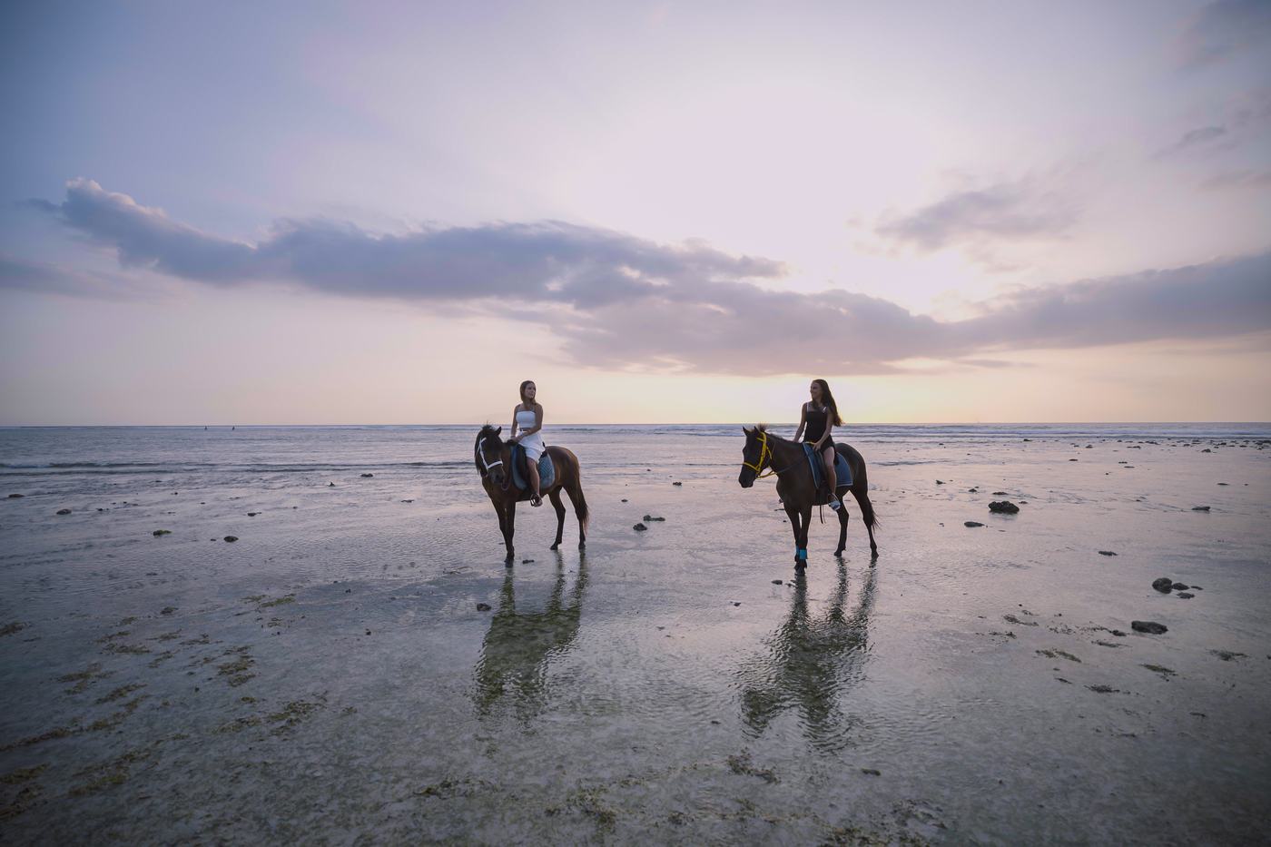 Two riders on horseback along the wet sand at sunset